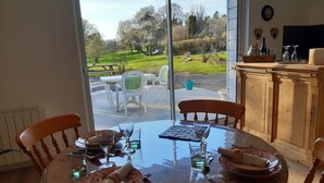Una mesa de comedor preparada para cuatro personas, con sillas, vista al jardín y un mueble de madera con utensilios de cocina.