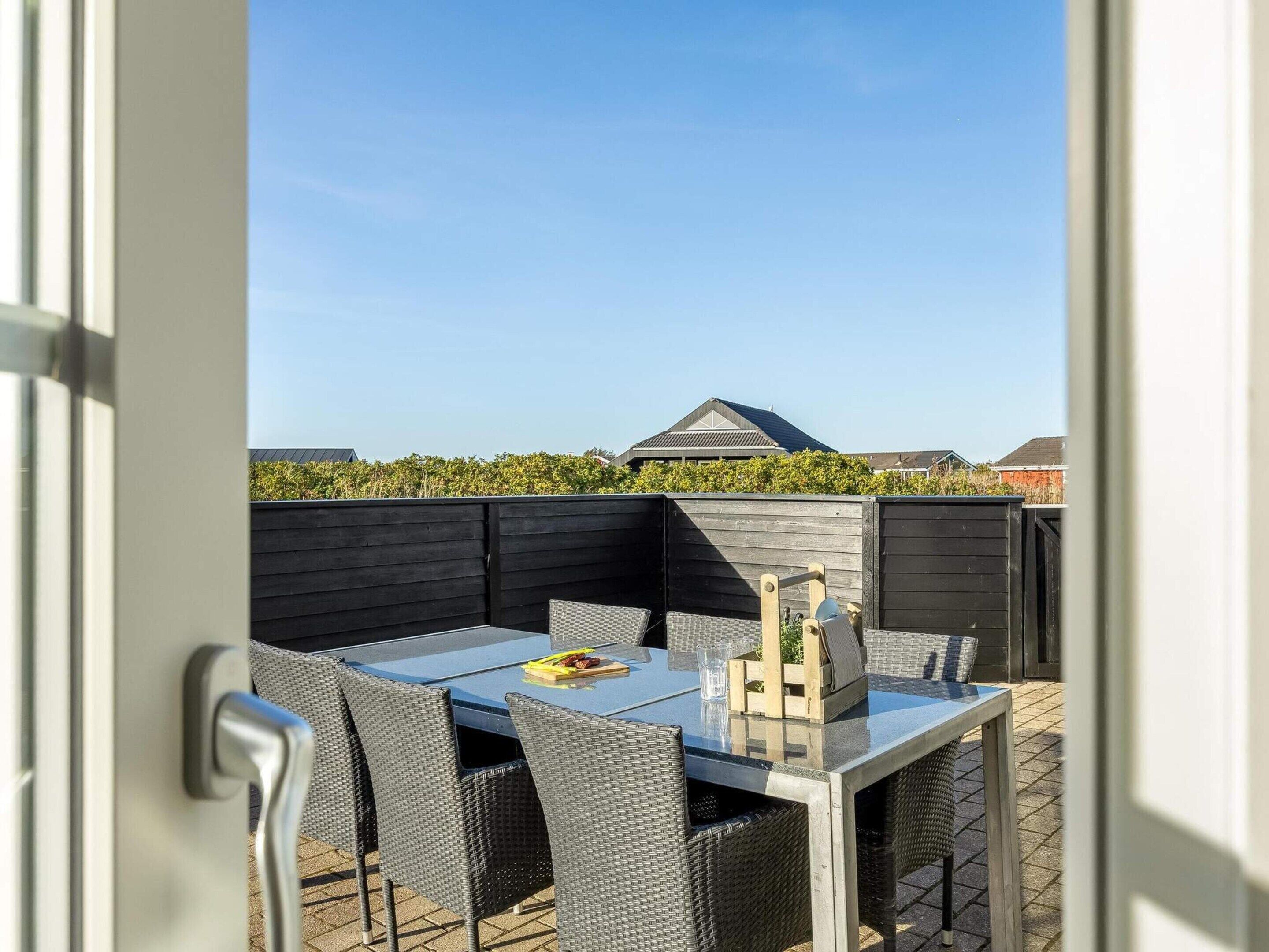 An outdoor patio with a table and chairs, a wooden fence, and a view of a house and trees.