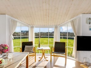 Ein Zimmer mit großem Fenster, einem Tisch, zwei Stühlen, einem Flachbildfernseher und einer Vase mit Blumen.
