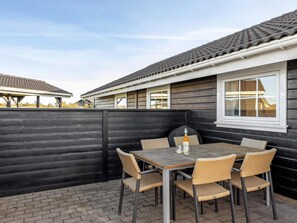 An outdoor patio with a table and chairs, a bottle of wine, and a wooden fence. - 4 Star Holiday Home in Lokken (Lokken)