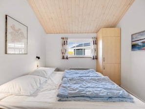 Ein Schlafzimmer mit einem Bett, einem Fenster mit Vorhängen, einer Holzbalkendecke und einem Kleiderschrank.