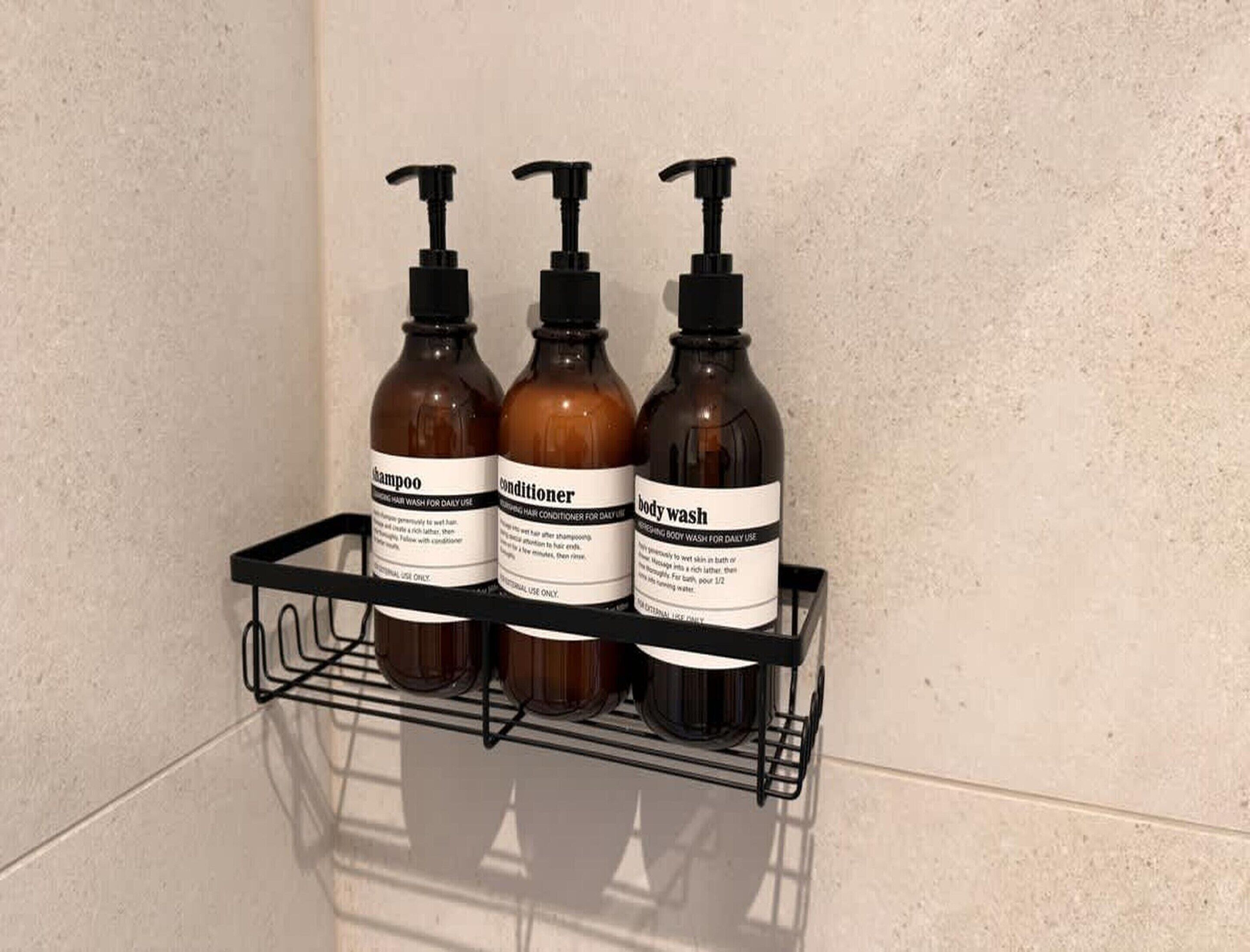 Une étagère de salle de bain contenant trois bouteilles de shampoing, d’après-shampoing et de gel douche.