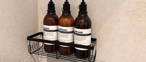 Une étagère de salle de bain contenant trois bouteilles de shampoing, d’après-shampoing et de gel douche.