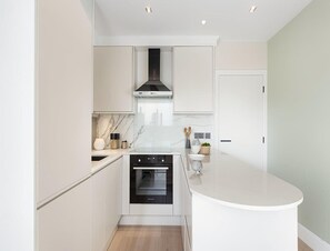 Uma cozinha moderna com armários brancos, forno embutido e bancada curva.