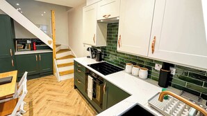 Una cocina moderna con armarios verdes, encimera blanca, pileta negra y escalera de madera.