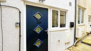 Una casa con puerta azul oscuro marcada con '34D', una ventana con persianas y una pared exterior blanca.