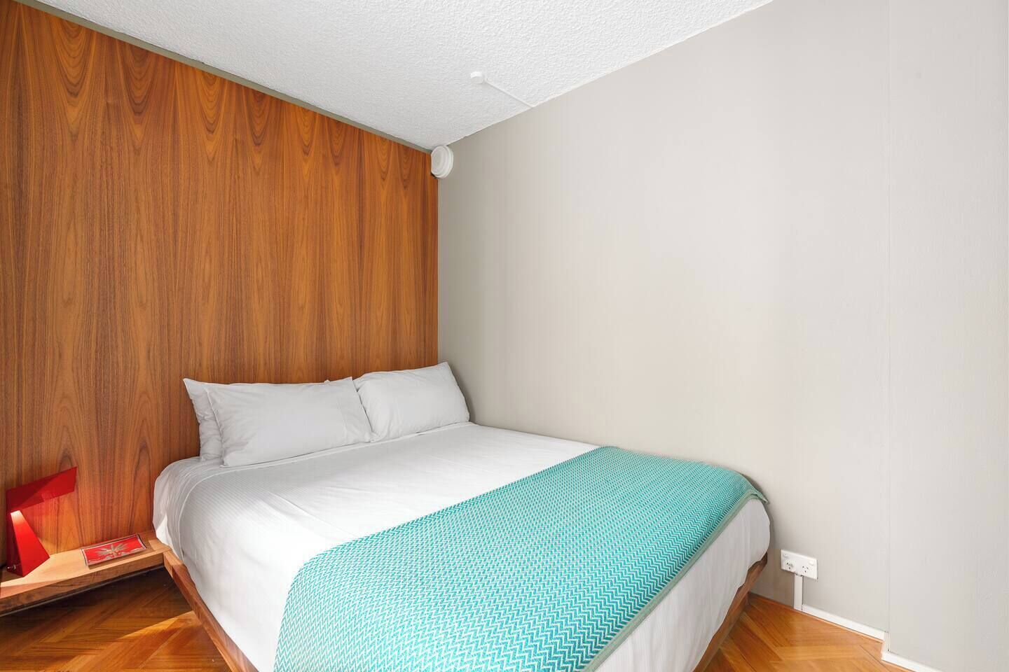 A bedroom with a wooden headboard, a bed with white bedding, and a teal-patterned throw blanket.