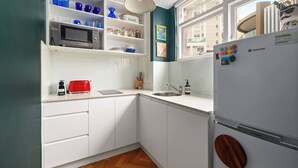 Una cucina compatta con mobili bianchi, un forno a microonde, un tostapane, un lavandino e un frigorifero.