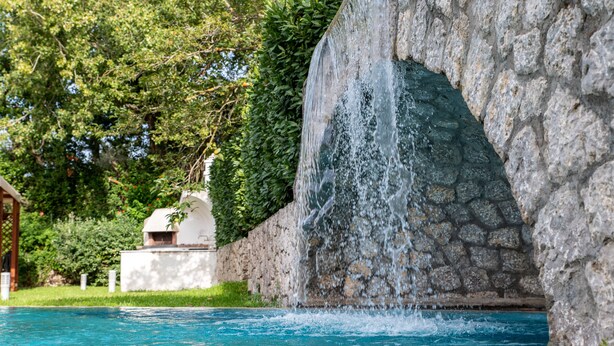 Una piscina con cascada, rodeada de muros de piedra y follaje.