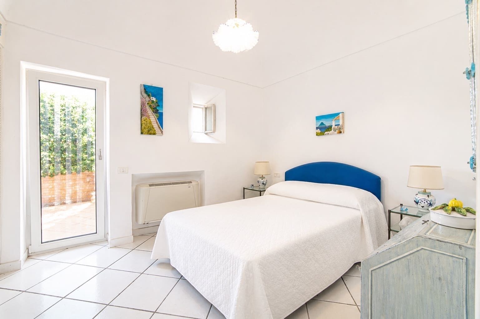 Un dormitorio con una cama, un radiador, una ventana y una puerta que da a un balcón.