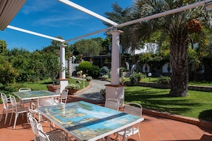 Eine Terrasse im Freien mit Tisch und Stühlen, umgeben von Grünpflanzen und einem Kiesweg.