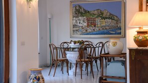 Un comedor con una mesa, sillas, un florero y un cuadro de un pueblo costero.