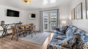 Una sala de estar con un sofá, una mesa de comedor con sillas, un televisor montado en la pared y un balcón con vistas.