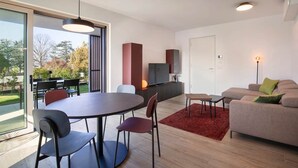 Ein modernes Wohnzimmer mit Essbereich, einer Couch, einem Fernseher und einem großen Fenster mit Blick auf Bäume.