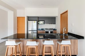 Eine moderne Küche mit schwarzer Arbeitsplatte, Edelstahlgeräten und Holzstühlen.