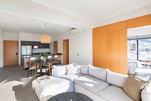Ein modernes Wohnzimmer mit einem großen weißen Sofa, einem Essbereich mit Tisch und Stühlen sowie einer Küche im Hintergrund.