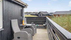 A balcony with wicker furniture, a bottle of alcohol, and a view of neighboring houses. - 4 Star Holiday Home in Lokken (Lokken)