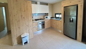 A compact kitchen with wooden cabinets, a microwave, a stove, a sink, and a refrigerator. - LUXURY APARTMENT IN THE BEACH (Punta Cana)