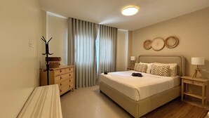 A hotel room with a bed, bedside tables, a dresser, a coat rack, and a window with curtains. - LUXURY APARTMENT IN THE BEACH (Punta Cana)