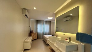 A modern bathroom with a large mirror, two sinks, a bench, and a walk-in shower. - LUXURY APARTMENT IN THE BEACH (Punta Cana)