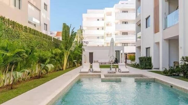 A swimming pool with lounge chairs, surrounded by greenery and modern buildings. - LUXURY APARTMENT IN THE BEACH (Punta Cana)