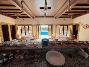 Ein Essbereich mit gedeckten Tischen, Blick auf einen Pool und eine Küchenzeile mit Kochutensilien.