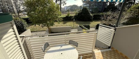 Un patio techado con una mesa y sillas, vista a un jardín y un edificio al fondo.