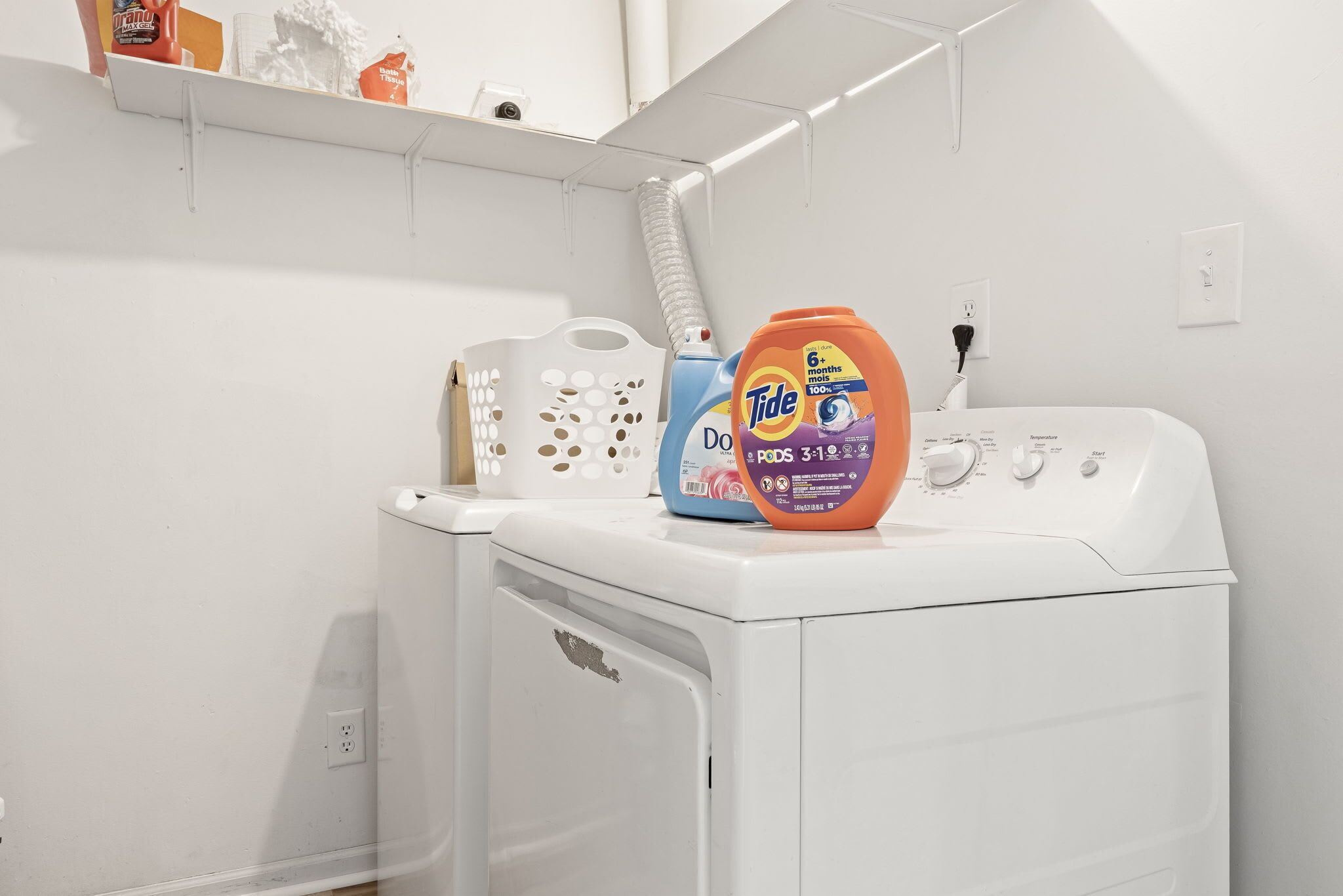 Etukuormattava pesukone, jossa on Tide-pesuainetta, ja valkoinen pyykkikori.