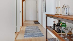 A hallway with wooden beams, a white door at the end, a rug, and a bar area with bottles and glasses. - 4 Star Holiday Home in Lokken (Lokken)