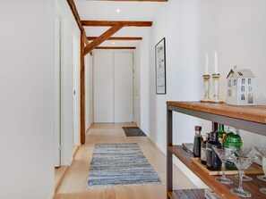 A hallway with wooden beams, a white door at the end, a rug, and a bar area with bottles and glasses. - 4 Star Holiday Home in Lokken (Lokken)