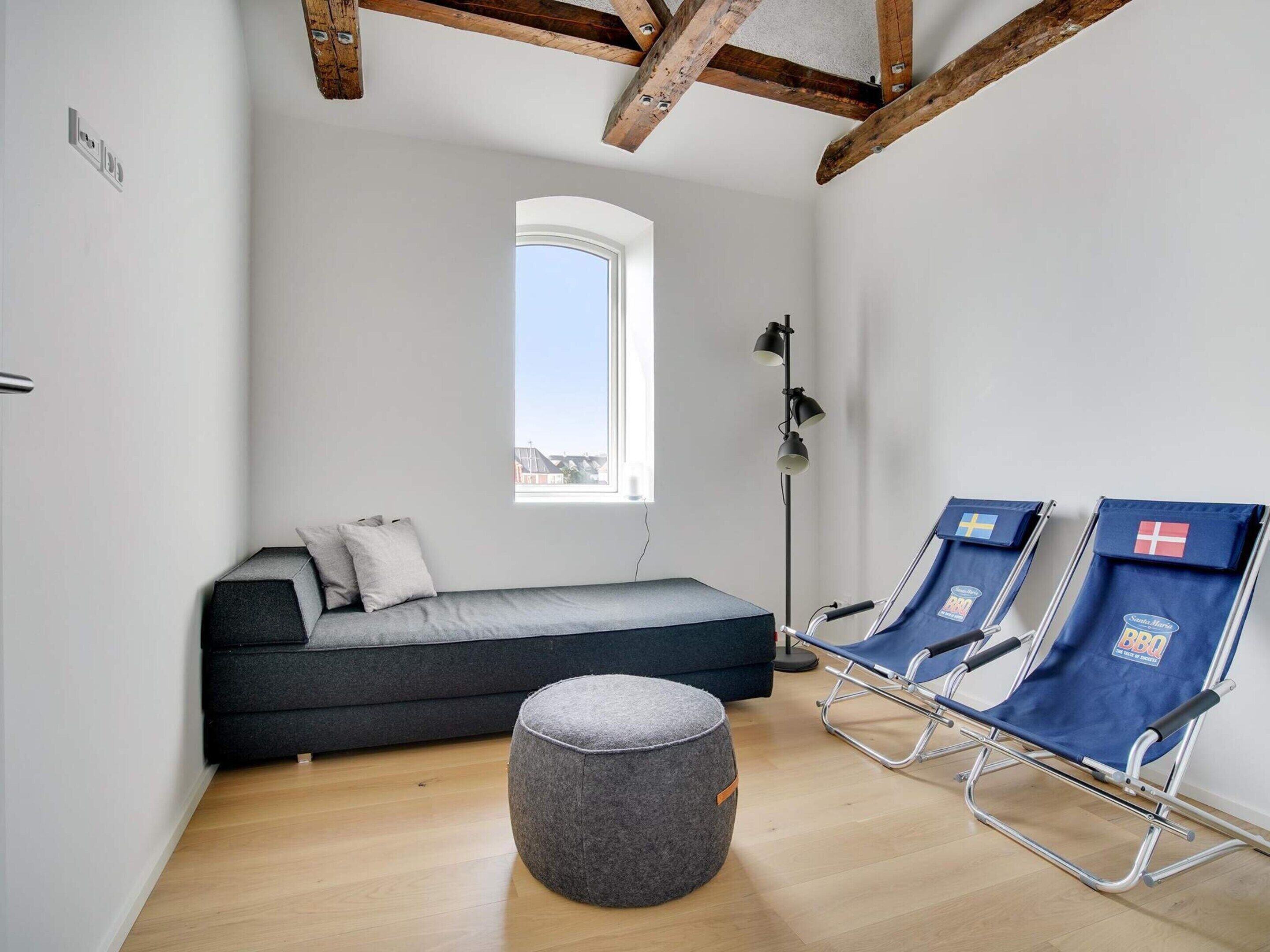Une pièce avec un lit en mezzanine, une petite fenêtre, une lampe sur pied et deux chaises bleues.