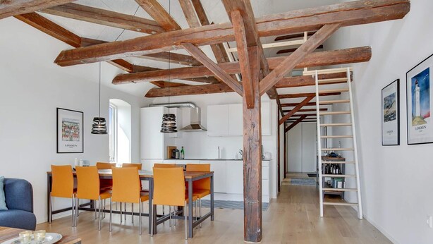 A spacious living area with a wooden ceiling, a dining table with orange chairs, a sofa, and a kitchen in the background. - 4 Star Holiday Home in Lokken (Lokken)