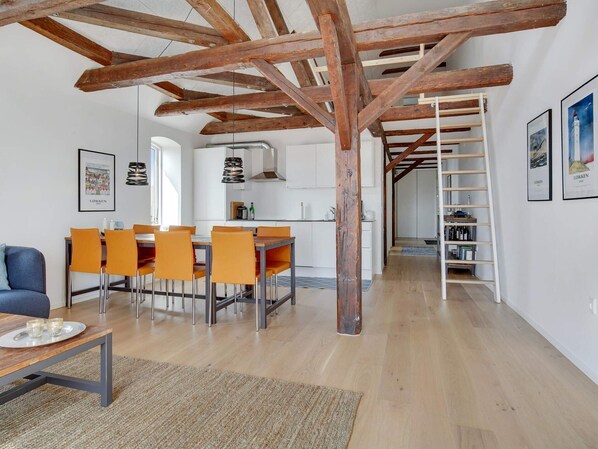 A spacious living area with a wooden ceiling, a dining table with orange chairs, a sofa, and a kitchen in the background. - 4 Star Holiday Home in Lokken (Lokken)