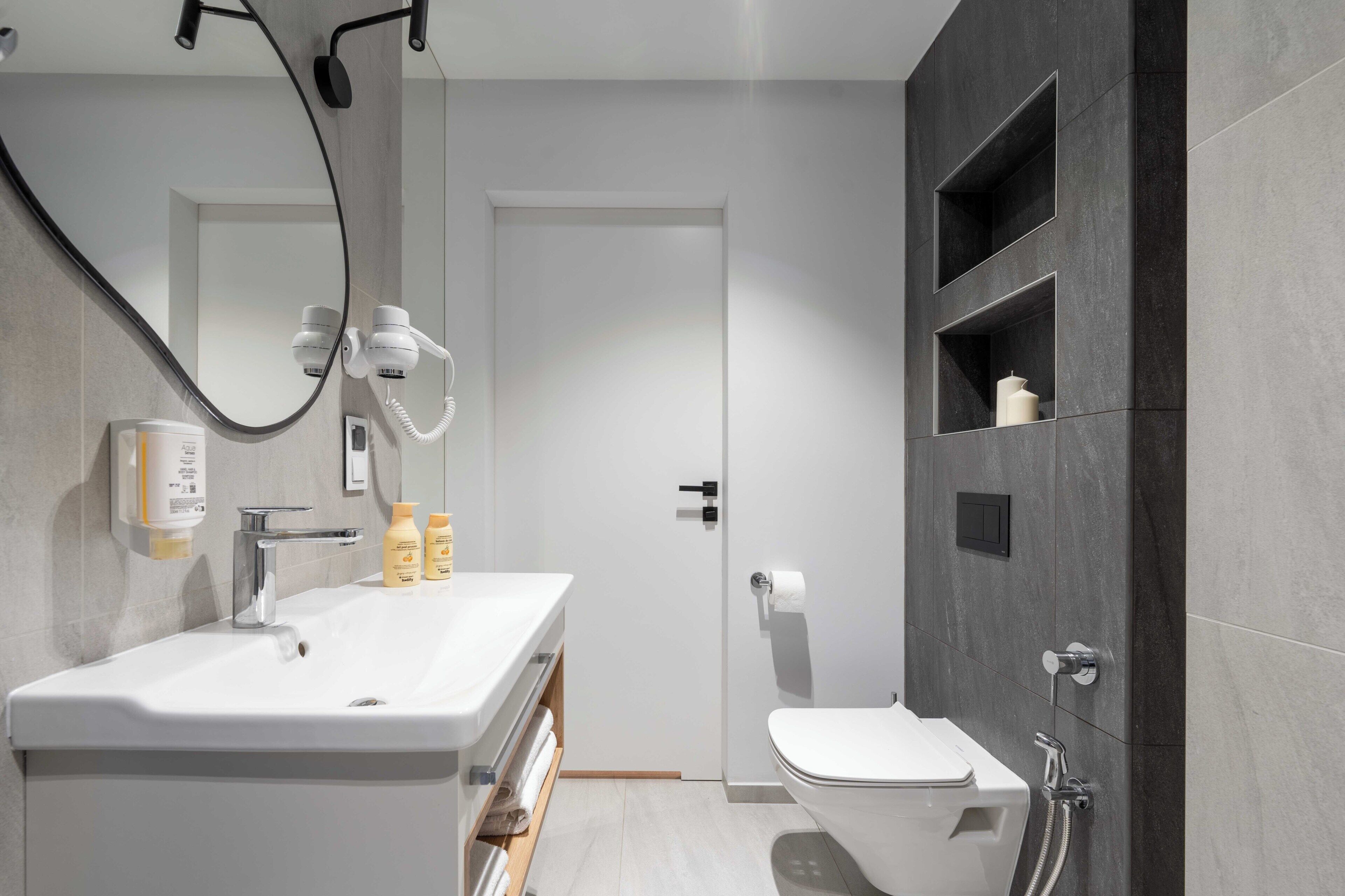 A modern bathroom with a white sink, mirror, and toilet.