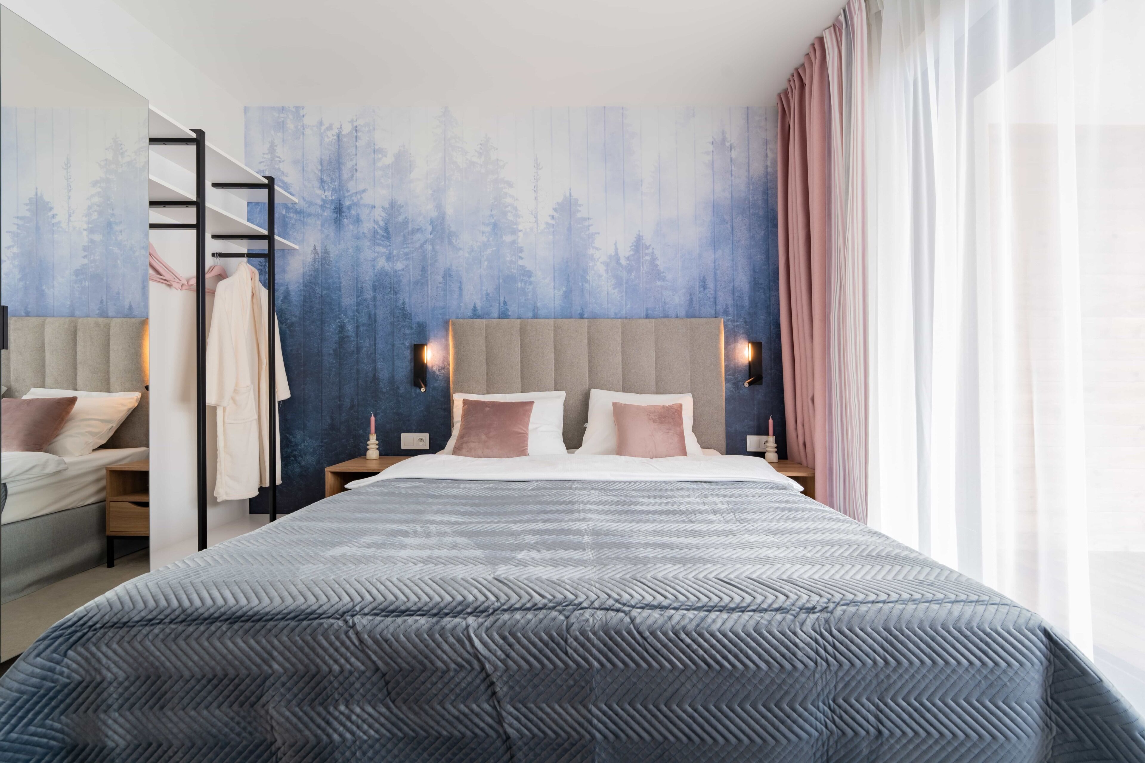 A modern bedroom with a large bed, a wardrobe, a nightstand, and a wall with a forest mural.