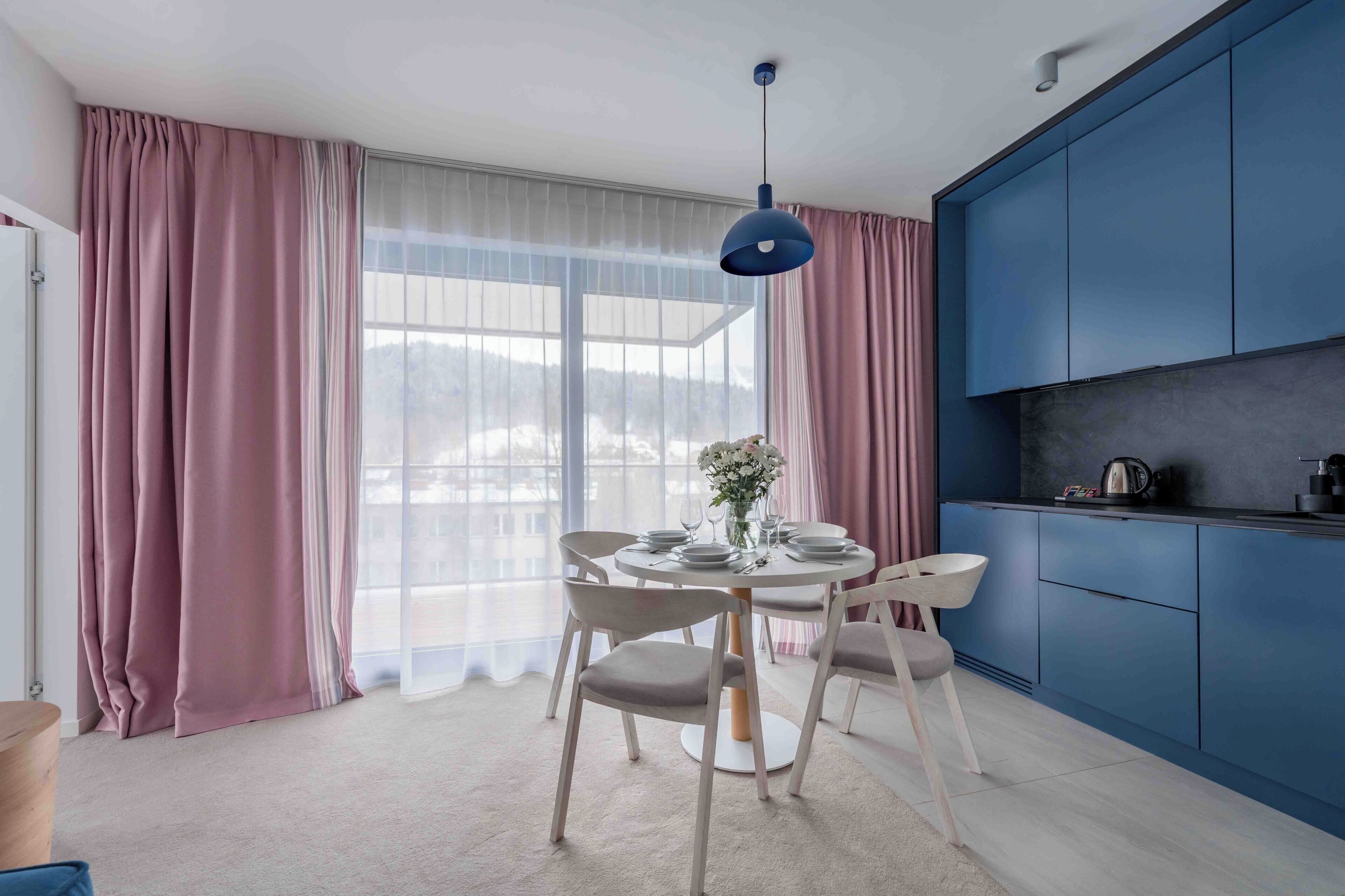 A modern kitchen with a dining area, featuring a round table, chairs, and a blue pendant light.