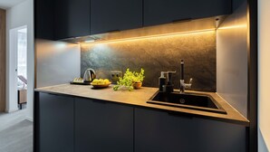 A modern kitchen with dark cabinetry, a stainless steel sink, and a countertop with a plant and a kettle.