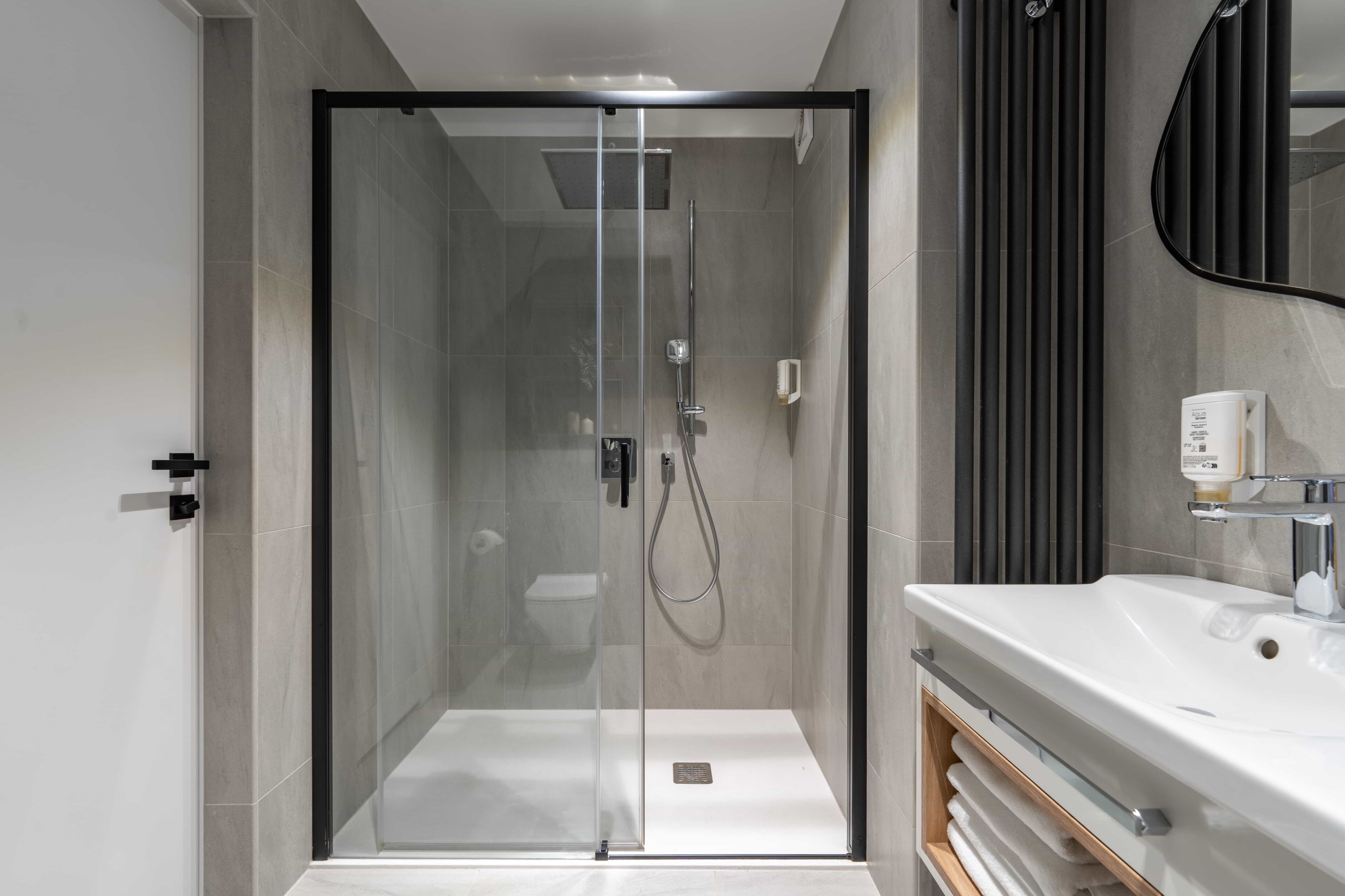 A modern bathroom with a glass-enclosed shower, a white sink, and a dark-toned mirror.