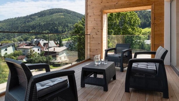 A balcony with wicker furniture, a glass table, and a view of a forested hill.