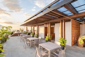 Eine Terrasses mit Tischen, Stühlen, einer Holzpergola und Blumentöpfen.