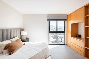 Ein Schlafzimmer mit Bett, Nachttisch, Lampe, Blick durch ein Fenster und Holzregalen.