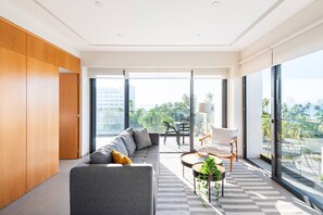 Ein modernes Wohnzimmer mit grauem Sofa, einem Holzschrank, einem Essbereich mit Tisch und Stühlen sowie großen Fenstern mit Blick auf die Stadt.