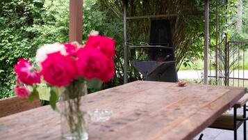 A wooden table with a vase of flowers, a grill, and a metal fence in a garden setting.
