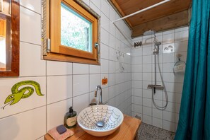 Une salle de bain avec un meuble-lavabo en bois, un lavabo agrĂ©mentĂ© dâun rĂ©cipient dĂ©coratif, une douche avec un pommeau de douche Ă main et une fenĂȘtre avec un cadre en bois.