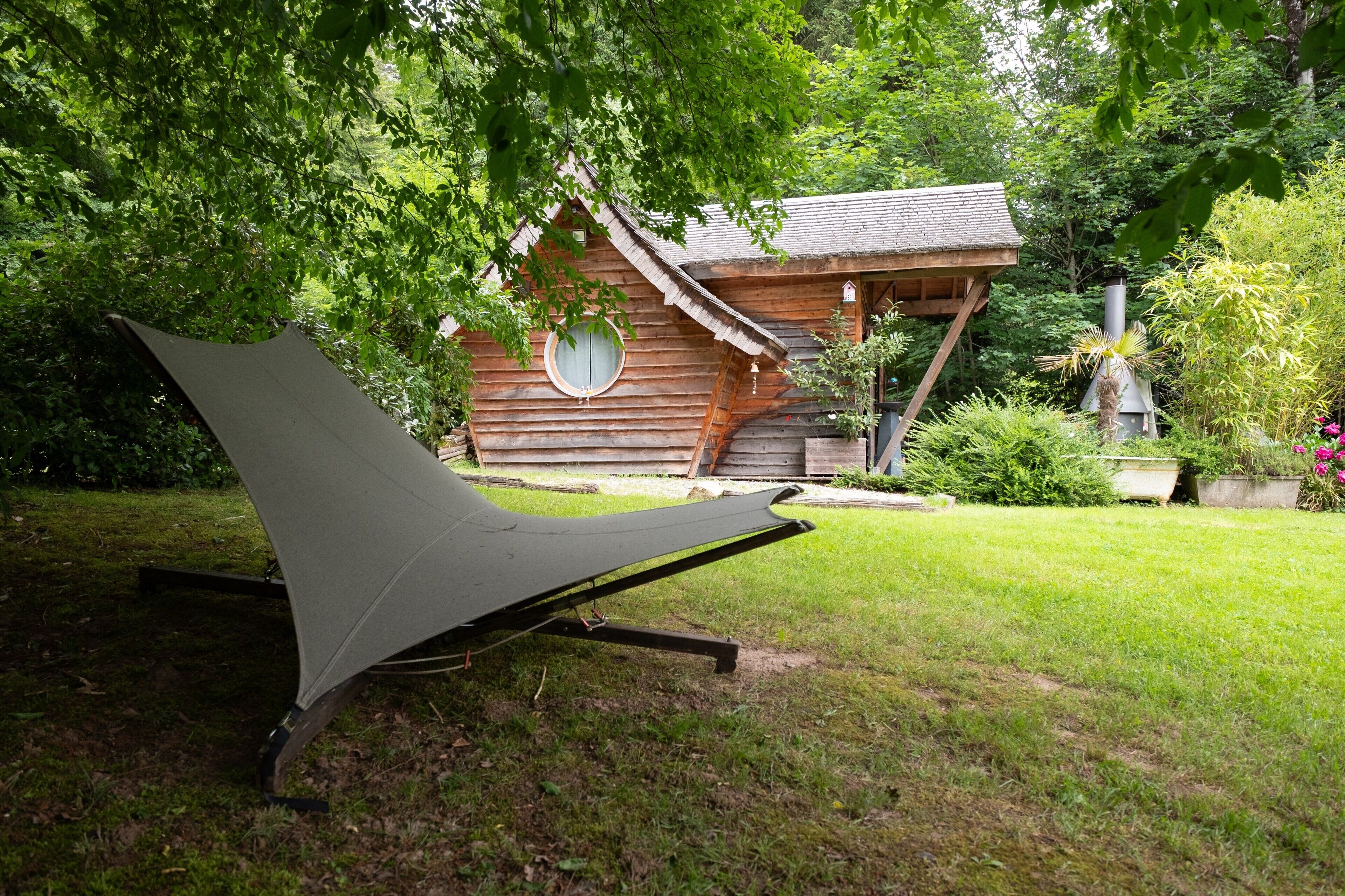 A hammock under a tree, a wooden cabin, and a garden with various plants.