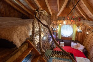 Une chambre mansardĂ©e chaleureuse avec un plafond en bois, un lit recouvert dâune couverture moelleuse, un petit coin salon avec des coussins et des guirlandes lumineuses.