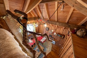 Un intérieur en bois agrémenté d’une balançoire en corde, d’un filet et d’un plafond rustique.