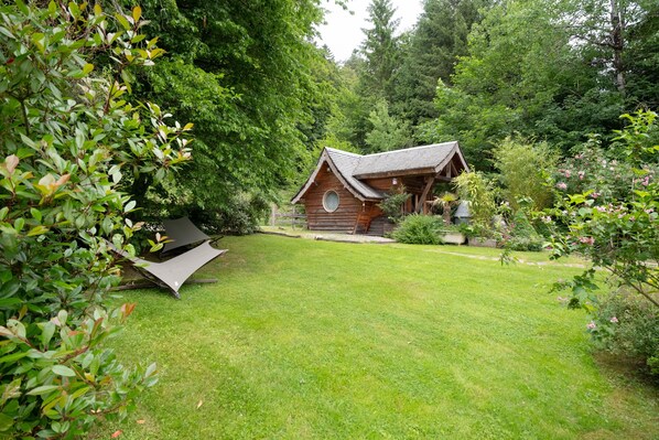 Une cabane en bois avec un toit Ă deux versants, entourĂ©e dâune vĂ©gĂ©tation luxuriante et dâune pelouse bien entretenue.