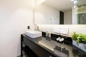 Casa de banho moderna com lavatório branco, bancada preta e um espelho grande.