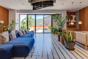 Eine moderne Hotelhalle mit einem blauen Sofa, Topfpflanzen und Blick auf die Stadt durch große Glasfenster.